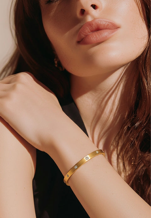 Close-up of a woman's wearing a B.Tiff BG308G matte 8-stone 18K gold plated bangle with a soft focus background