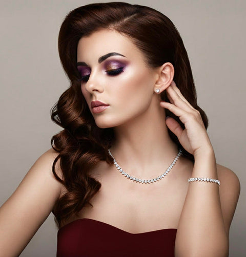 Woman wearing B.Tiff heart tennis necklace C102W, BG399W heart tennis bracelet, ER009W heart diamond earrings in a elegant burgundy gown with a neutral background