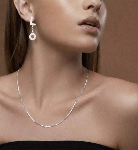 Close-up of a woman wearing a B.Tiff C002W silver necklace and B.Tiff ERloveW silver "LOVE" letters earrings showing the side of the linked letters "L" and "O" against a neutral background