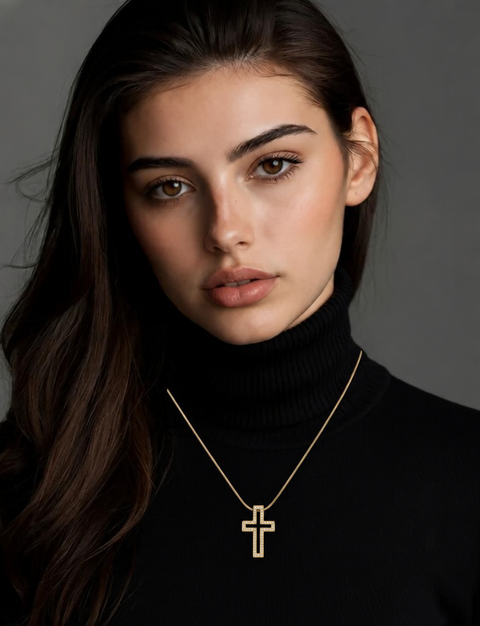 A close-up of a woman with long dark hair wearing a delicate B.Tiff PT098G gold cross pendant necklace over a black turtleneck sweater, set against a dark gray studio background.
