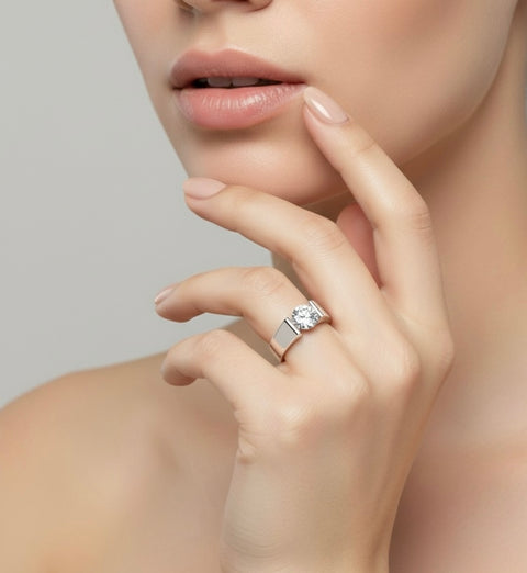 Close-up of a woman's hand wearing a B.Tiff RG093W ring tension set with a 2 carat round solitaire diamond alternative on top with a neutral background