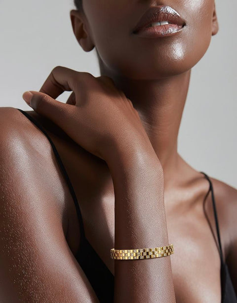 Close-up of a woman's arm wearing a B.Tiff BG104G trellis 18K gold plated bangle bracelet against a neutral background