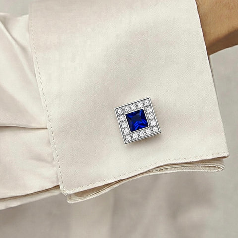 Cufflink with a blue gemstone and clear stones on a white cuff against a beige background