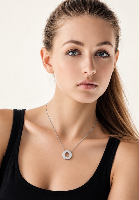 A close-up of a woman wearing a delicate B.Tiff PT100W silver pendant necklace with a circular openwork design, paired with a black tank top against a light off-white background.