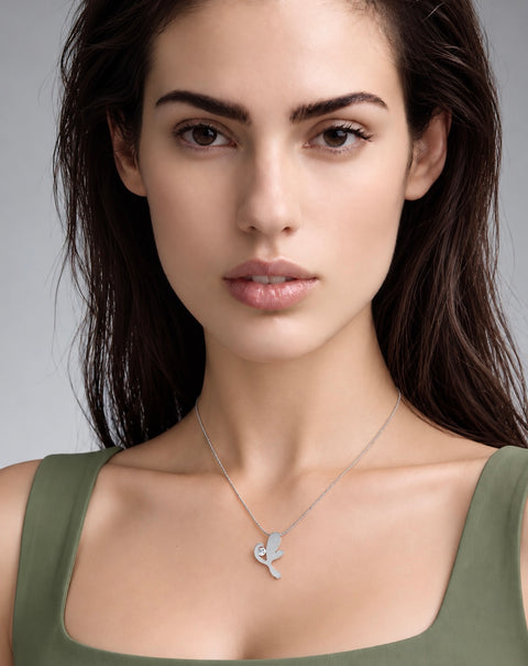 A close-up portrait of a woman wearing a delicate B.Tiff PT102W silver pendant necklace with a stylized clover design, paired with an olive green top against a neutral gray background.
