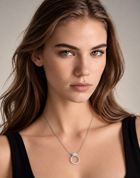 A close-up portrait of a woman wearing a delicate B.Tiff PT117W silver ring pendant necklace with a small clear gemstone, styled with a black top against a neutral gray background.